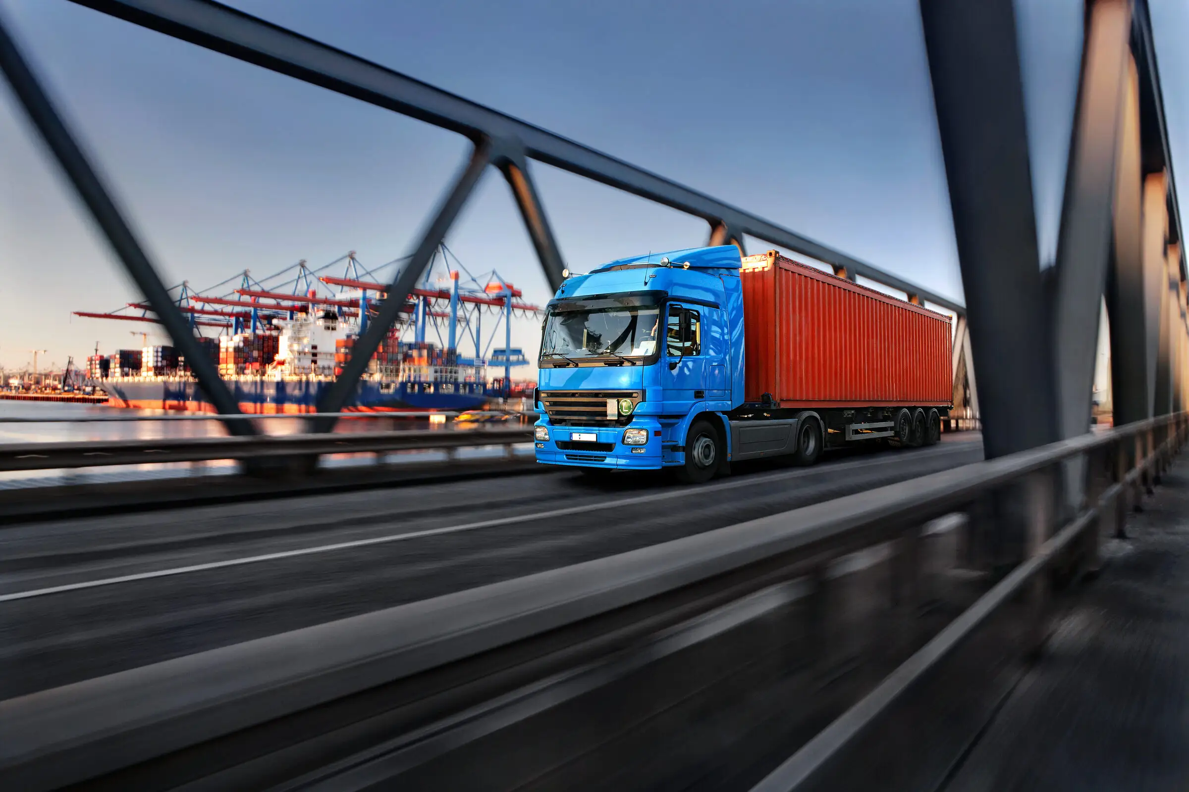 Blauer Lkw auf einer Brücke vor einem Containerhafen